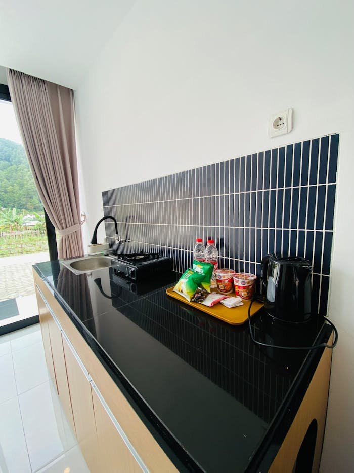 Contemporary kitchenette with cooker, kettle, and snacks by a window.