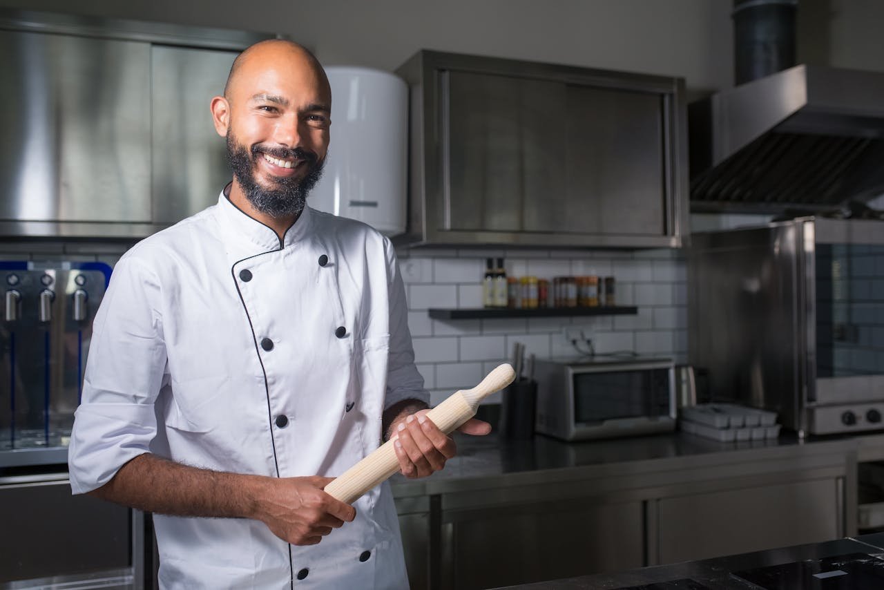 Chef in a modern kitchen holding a rolling pin, ready for cooking with a confident smile.