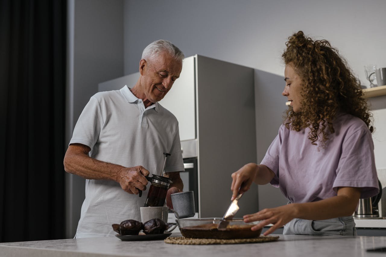 Senior man and young woman laughing while preparing cake in a cozy kitchen.